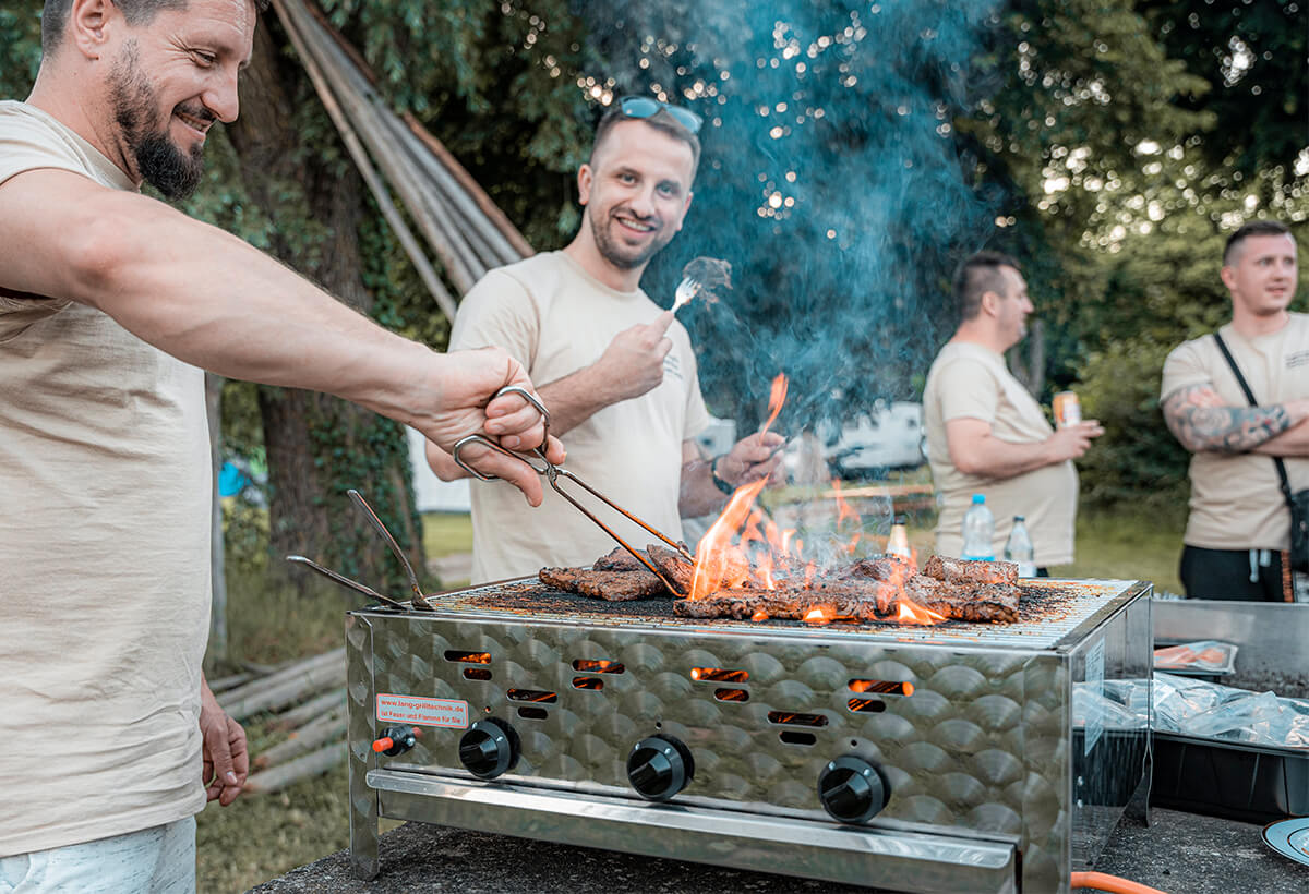 Mitarbeiter der Gronover Elektrotechnik stehen gemeinsam vor einem Grill und braten Steaks